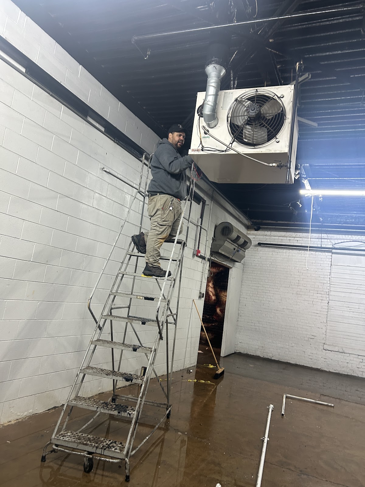 A Hoosier Man tech on a ladder servicing a ceiling heater