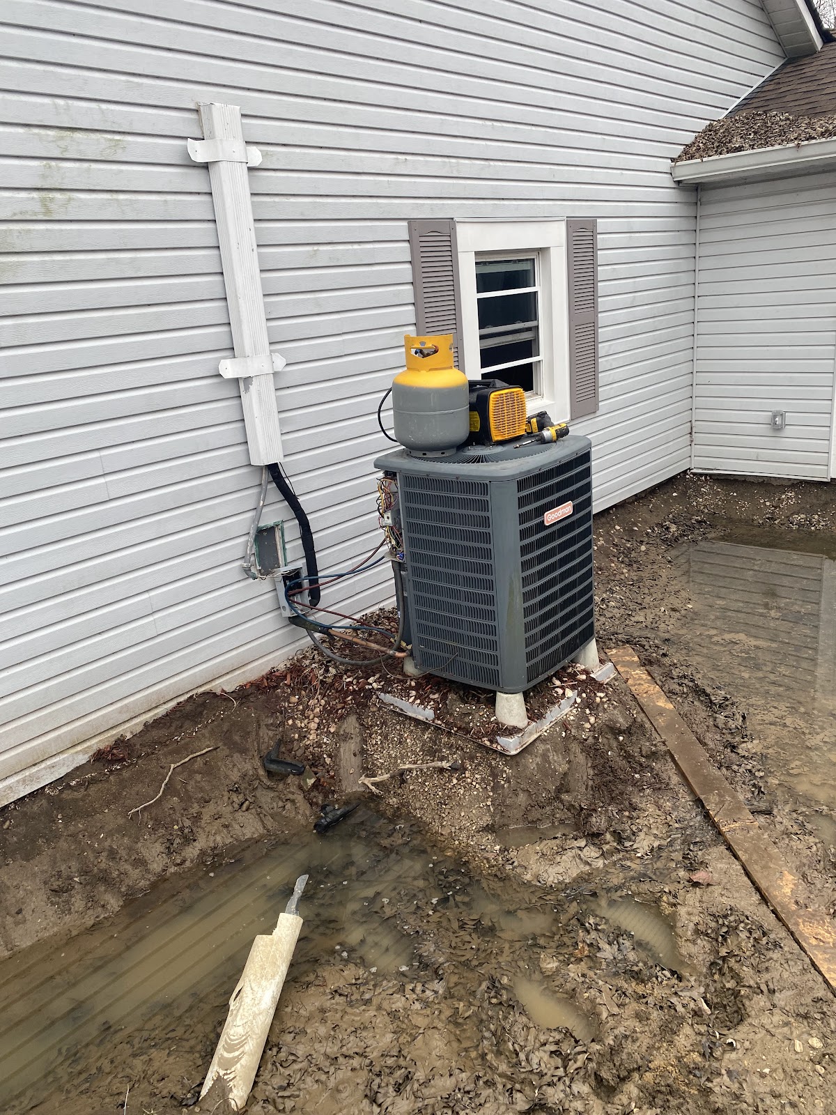 An outdoor AC unit being recharged on a muddy job site